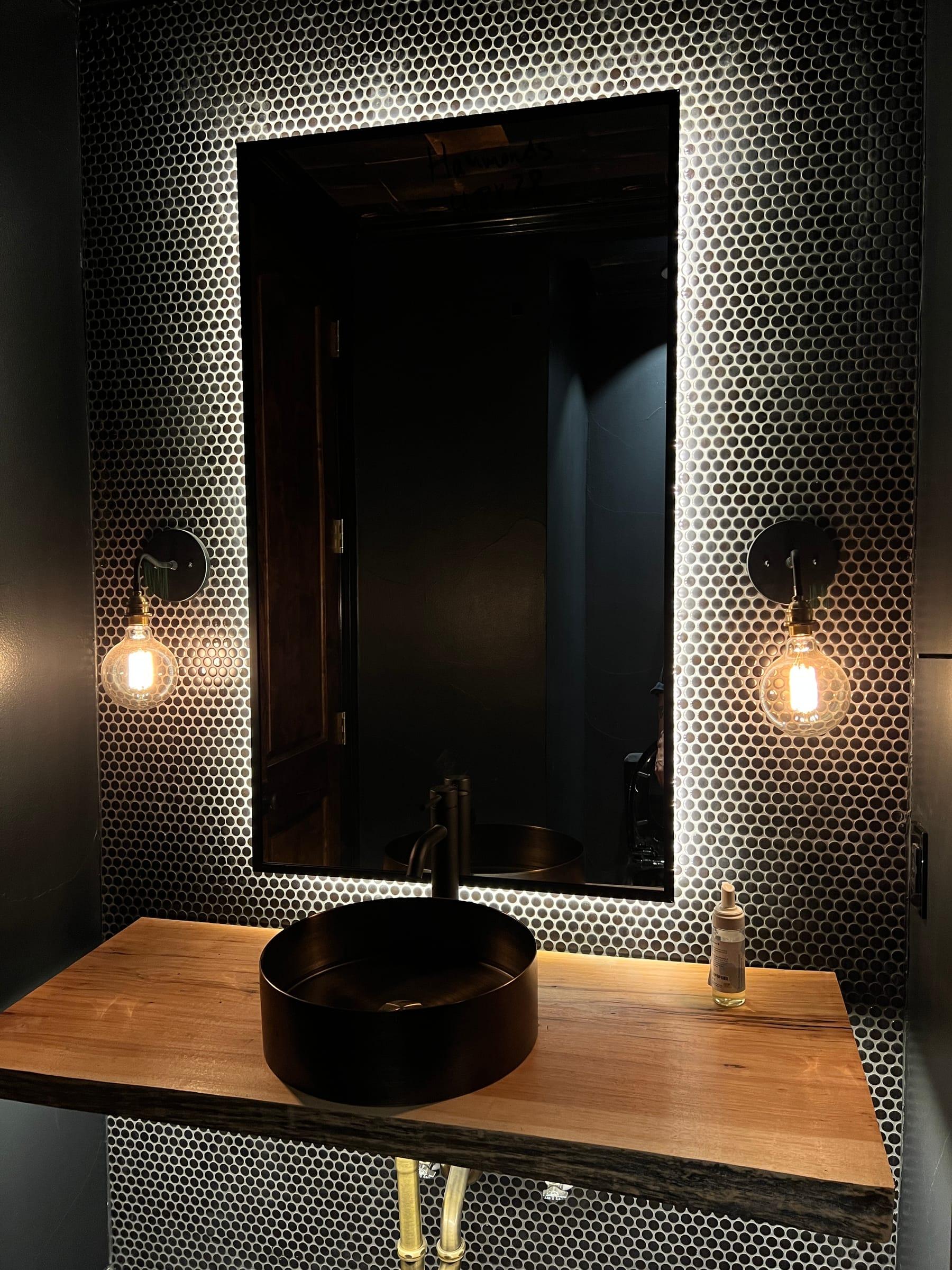 Powder room with a halo-backlit mirror, Edison sconces, and a live-edge floating vanity.