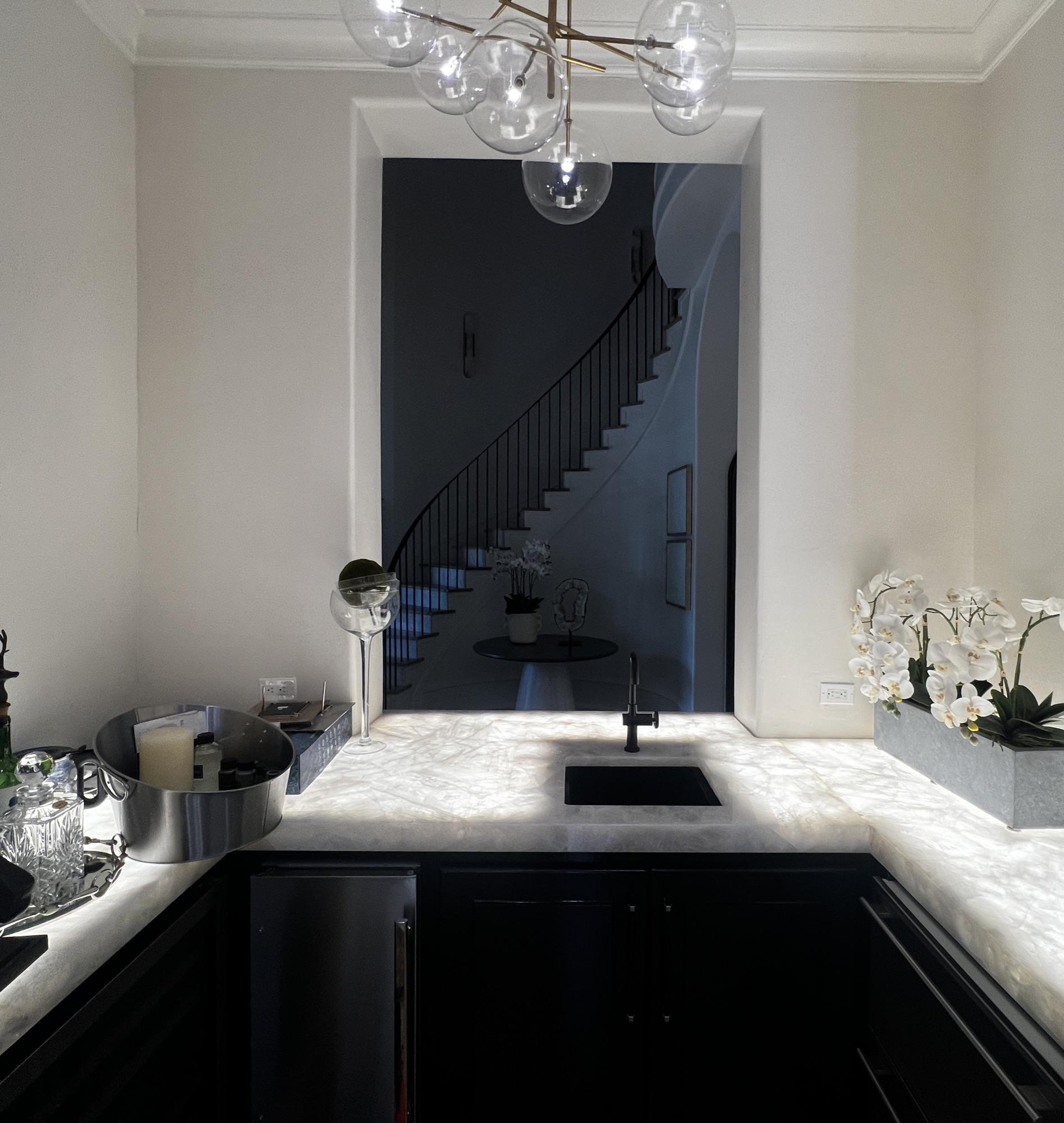 Butler's pantry with a backlit quartzite counter glowing from under-cabinet LED, staircase beyond.