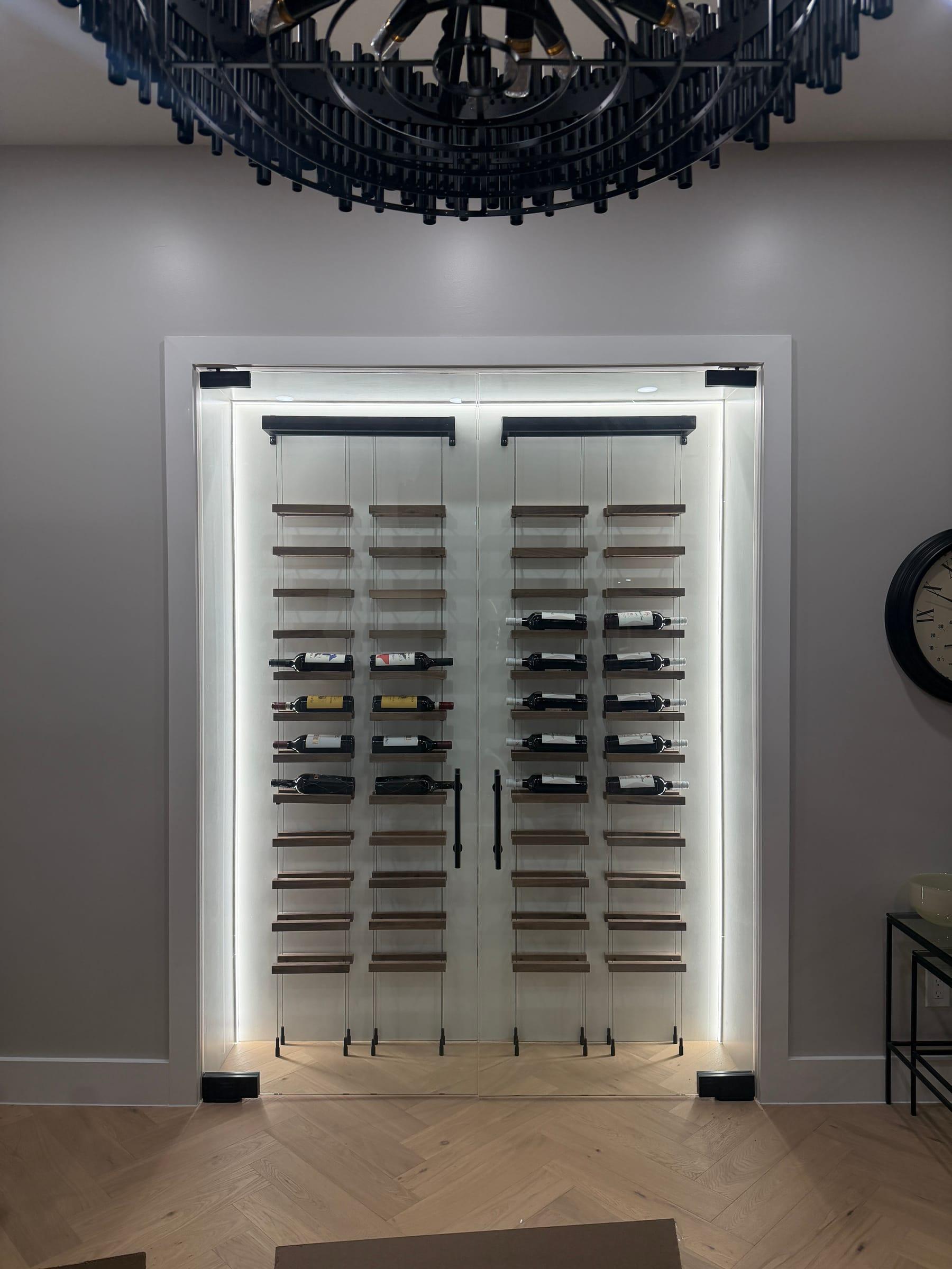 Glass-enclosed wine room with LED-lit display shelving under a drum chandelier.